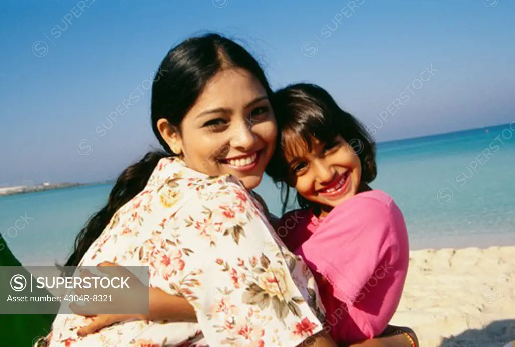 Mother and daughter hug each other as they smile at the camera.