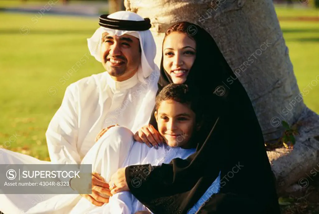 An Arabian family shares a light moment as they sit under the tree and smile.