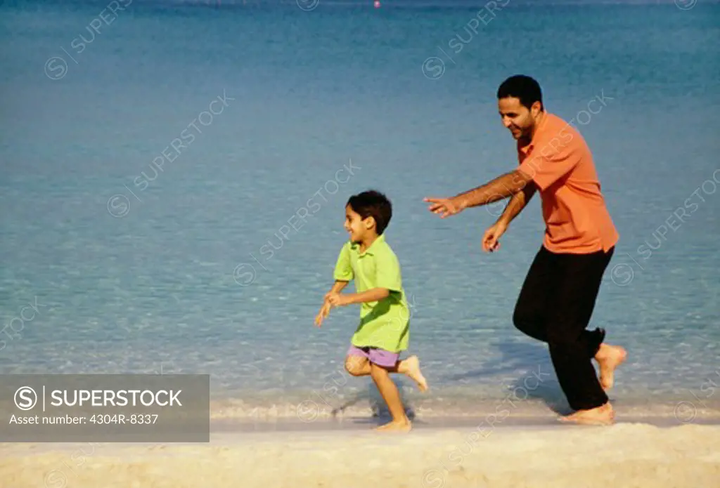 A father runs behind his son as they enjoy playing at the beach.