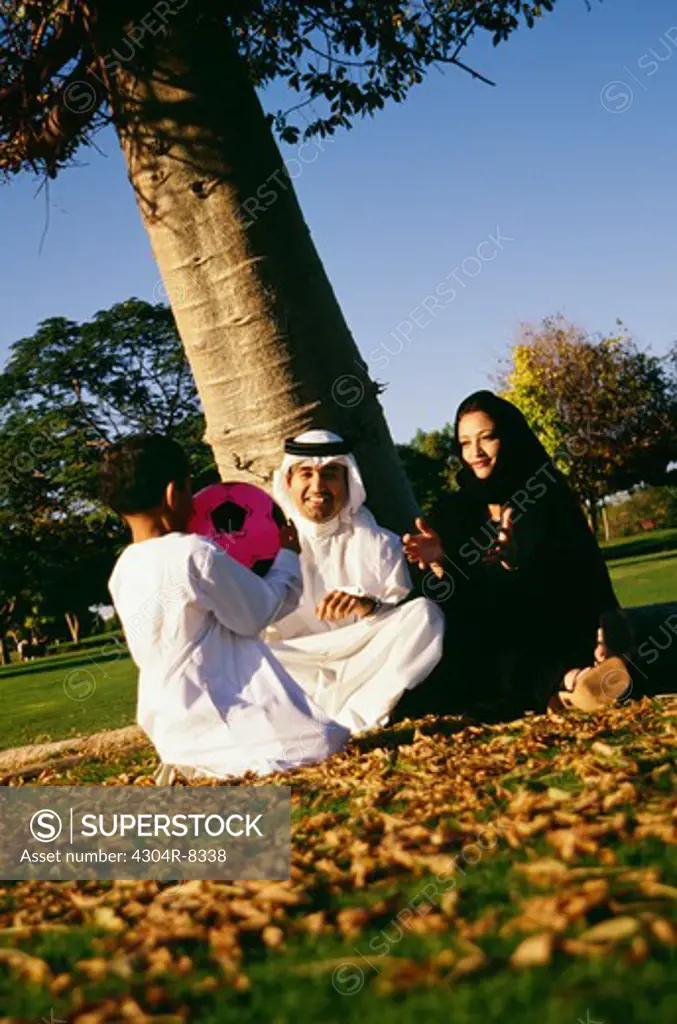 An Arabian family shares a light moment as they sit under the tree and smile.