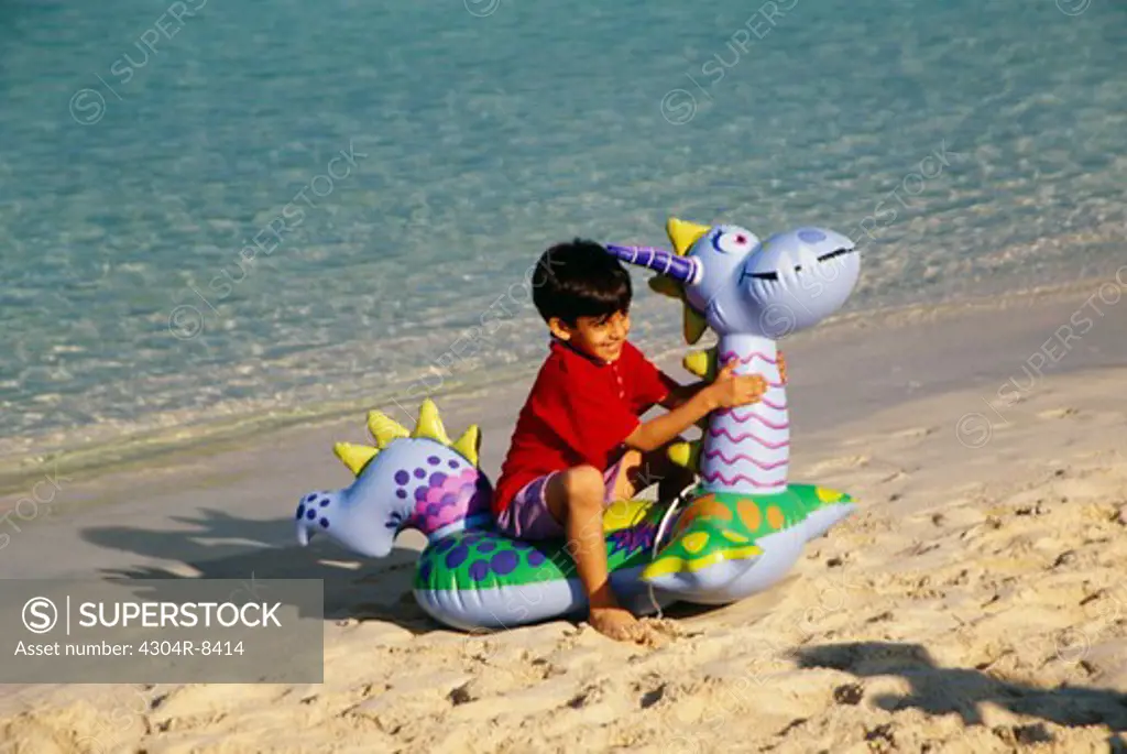 A small boy sits on an air filled toy as he enjoys at the beach.