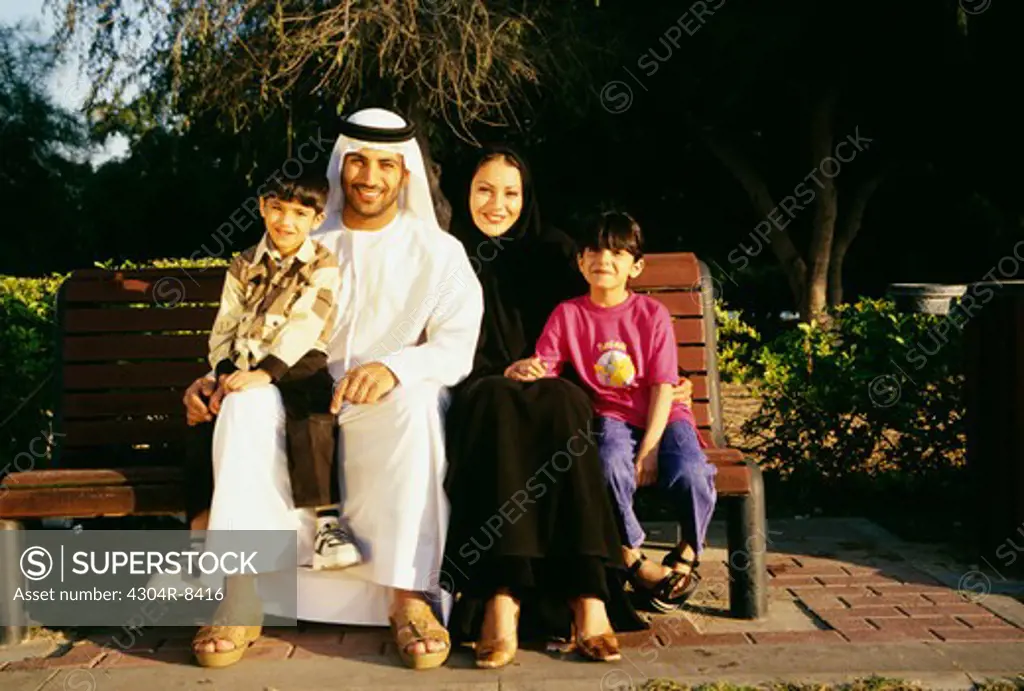 A family smiles at the camera as they are seated on the bench.