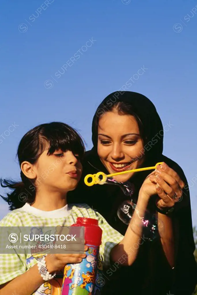 A girl blows off the soap bubble while the mother holds her hand.