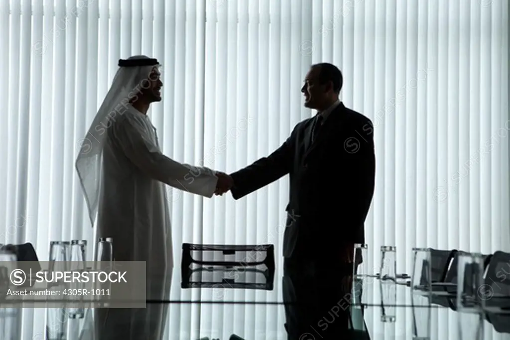 Silhouette of two businessmen shaking hands in a conference room.