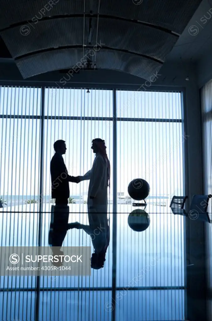 Silhouette of two businessmen shaking hands in a conference room.