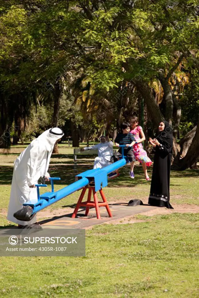 Multi-generation arab family at the park, children riding on the seesaw.