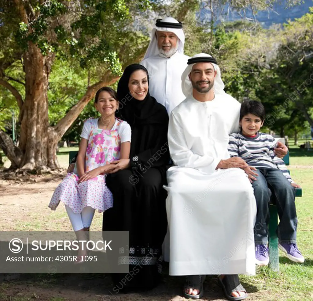 Portrait of multi-generation arab family sitting on bench at the park, smiling.