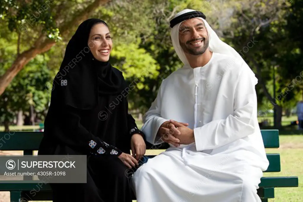 Arab couple sitting at the park, smiling.