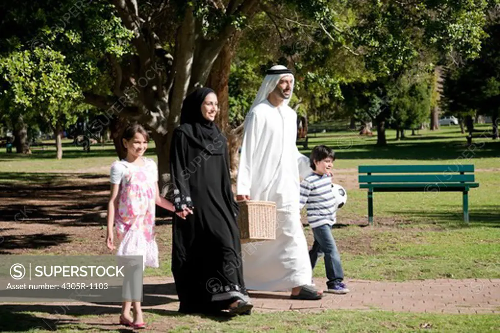 Arab family with picnic basket holding hands while walking at the park.