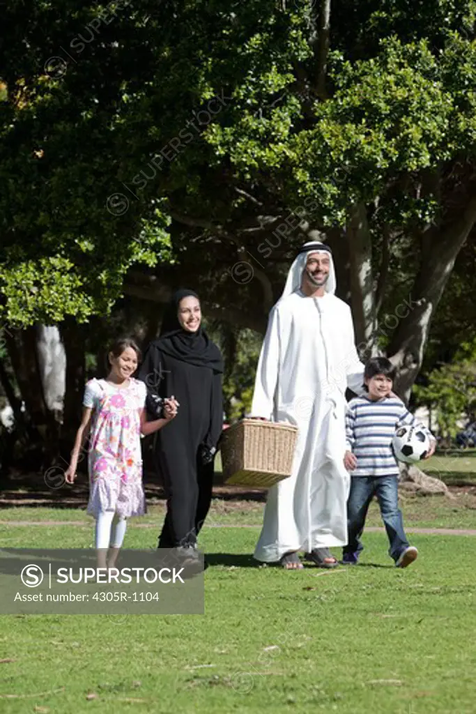 Arab family with picnic basket holding hands while walking at the park.