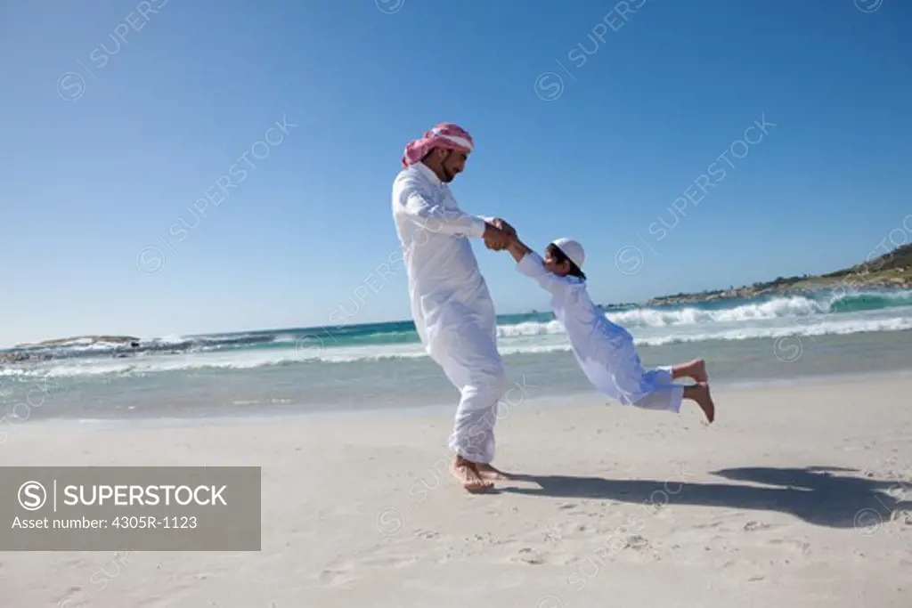 Arab father spinning his son around at the beach.