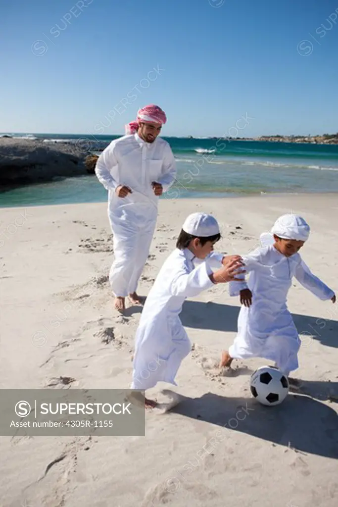 Arab father with two sons playing soccer ball by the beach.