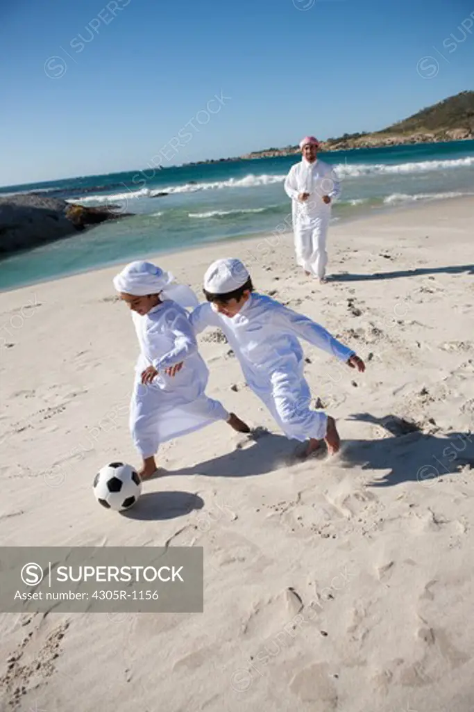 Arab father with two sons playing soccer ball by the beach.