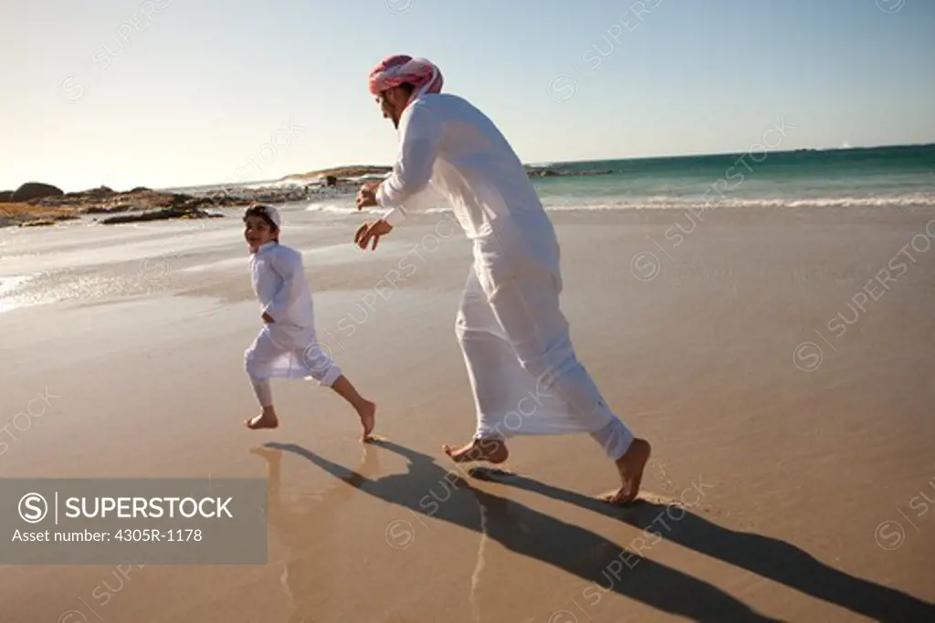 Arab father and son running at the beach.