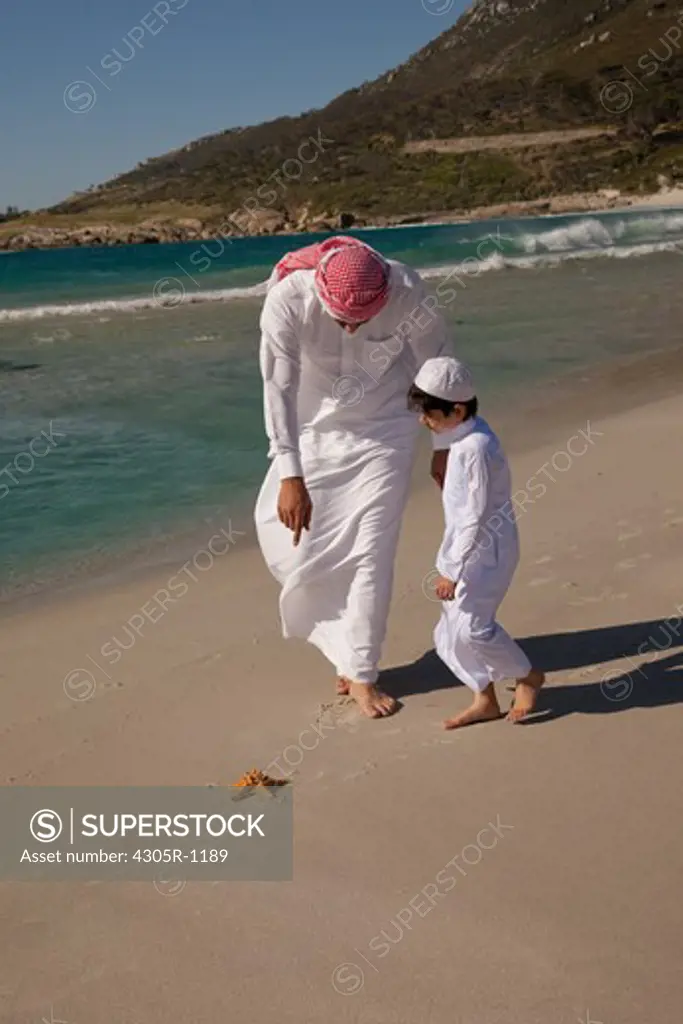 Arab father and son looking at a starfish on the beach.