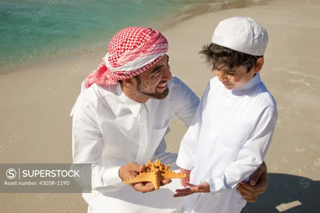Arab father and son with starfish at the beach.