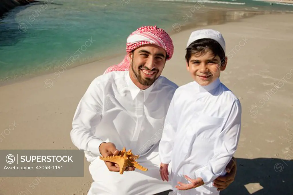 Arab father and son with starfish at the beach, smiling.