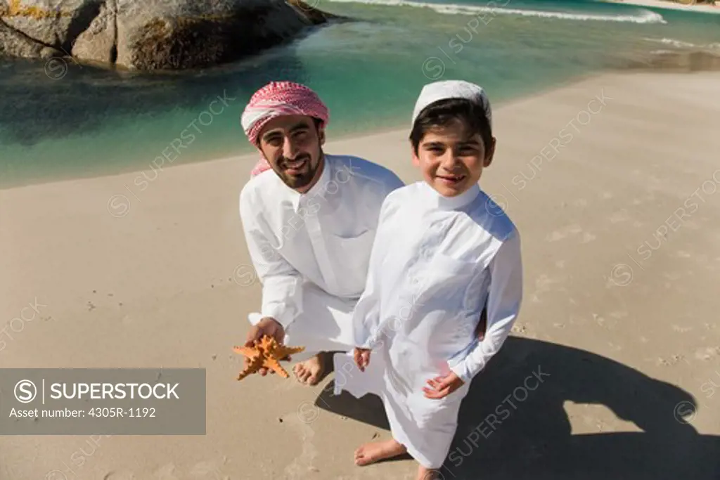 Arab father and son with starfish at the beach, smiling.