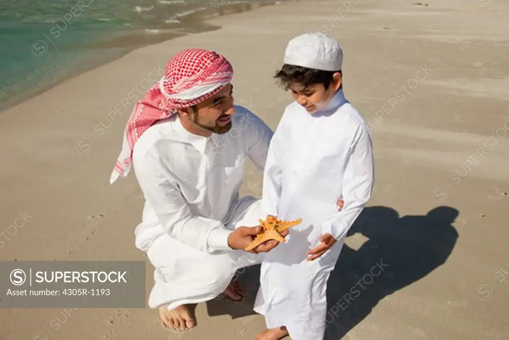 Arab father and son with starfish at the beach.