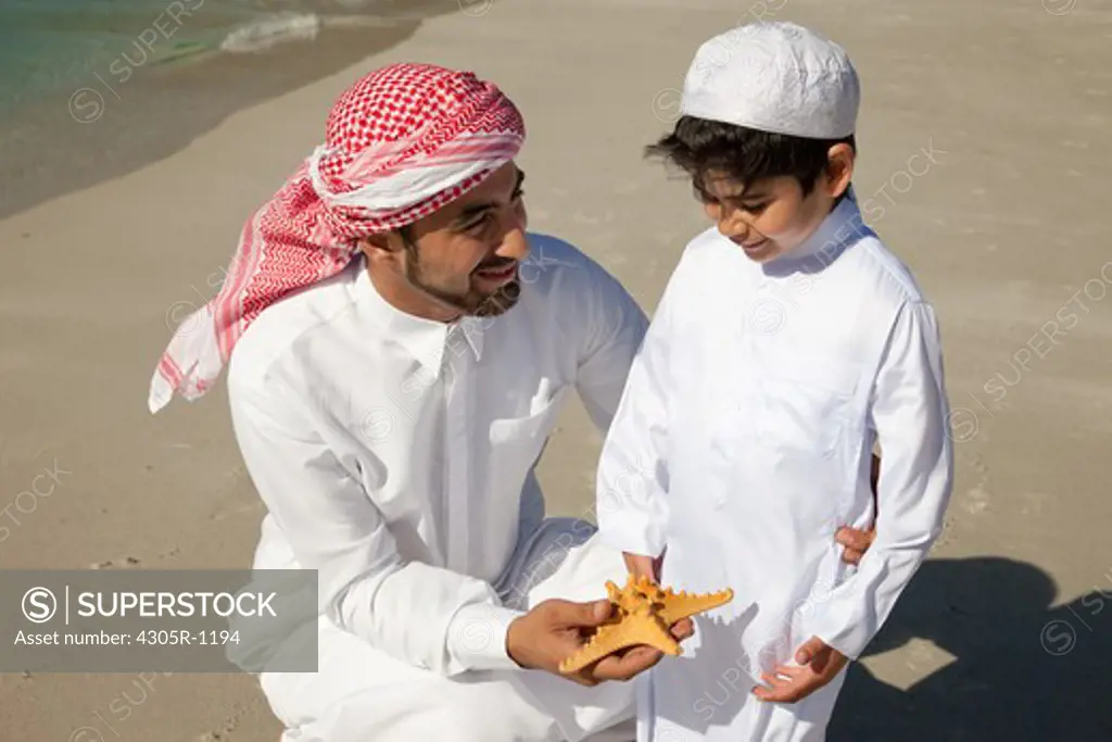 Arab father and son with starfish at the beach.