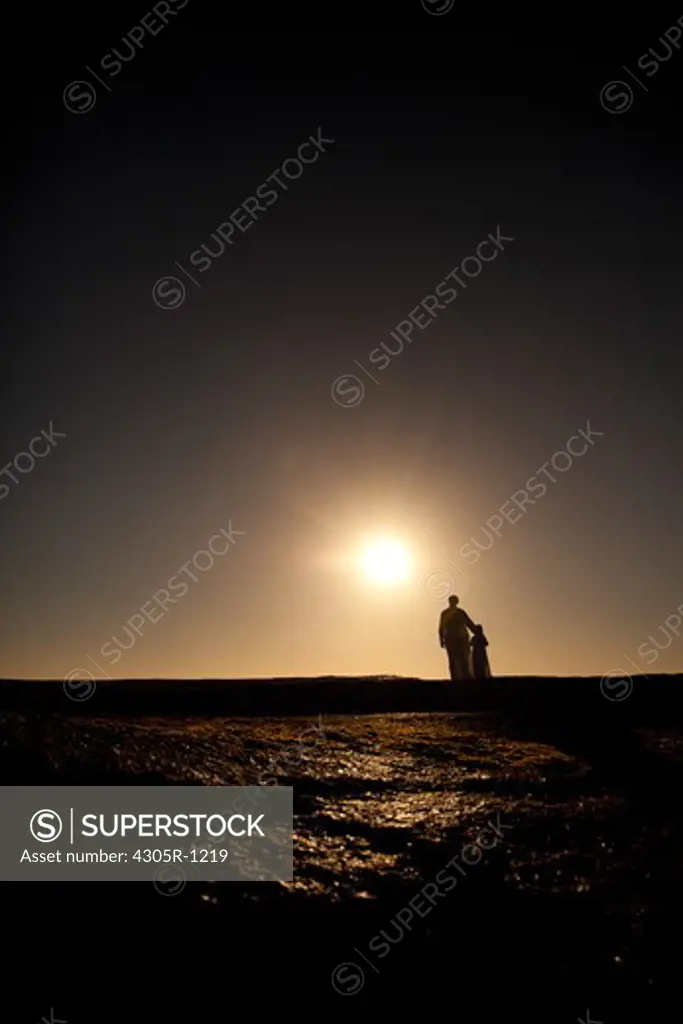 Silhouette of an arab father and son standing on cliff by the beach.