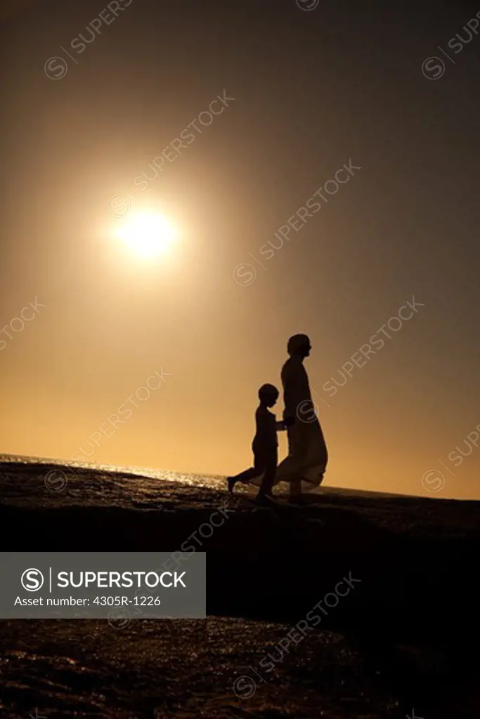 Silhouette of an arab father and son walking on cliff by the beach