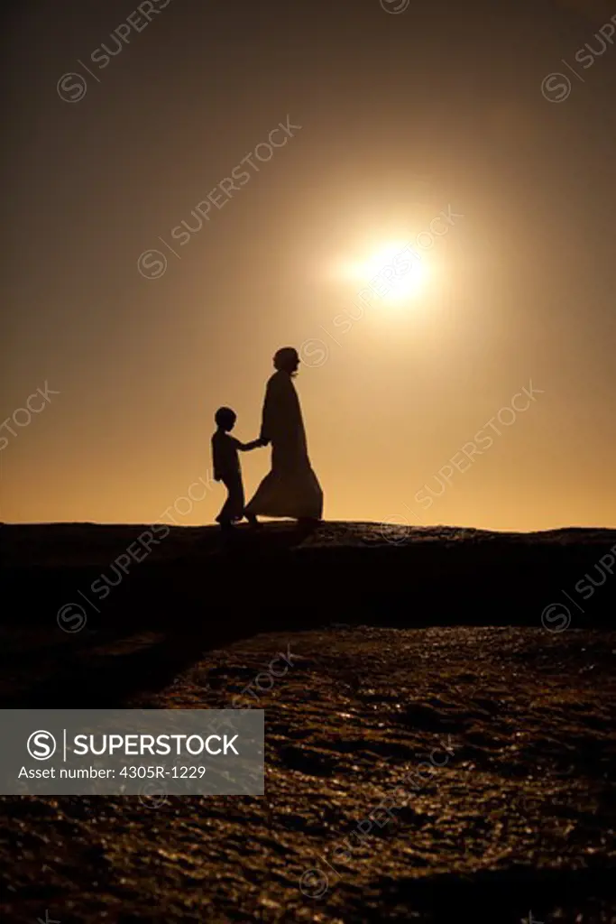 Silhouette of an arab father and son walking on cliff by the beach