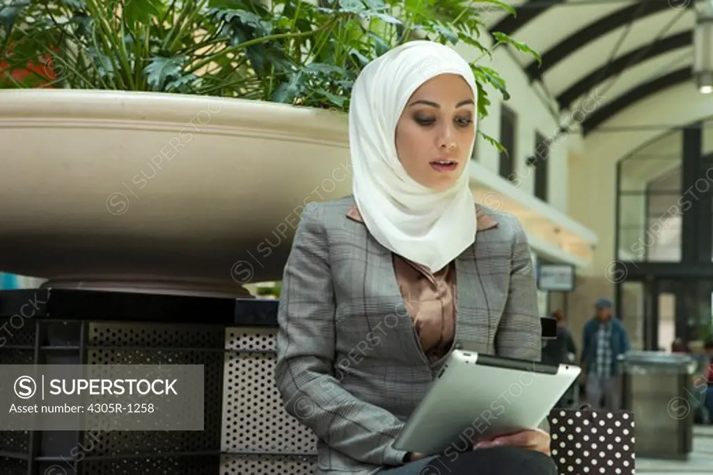 Young arab woman with digital tablet sitting at the shopping mall.