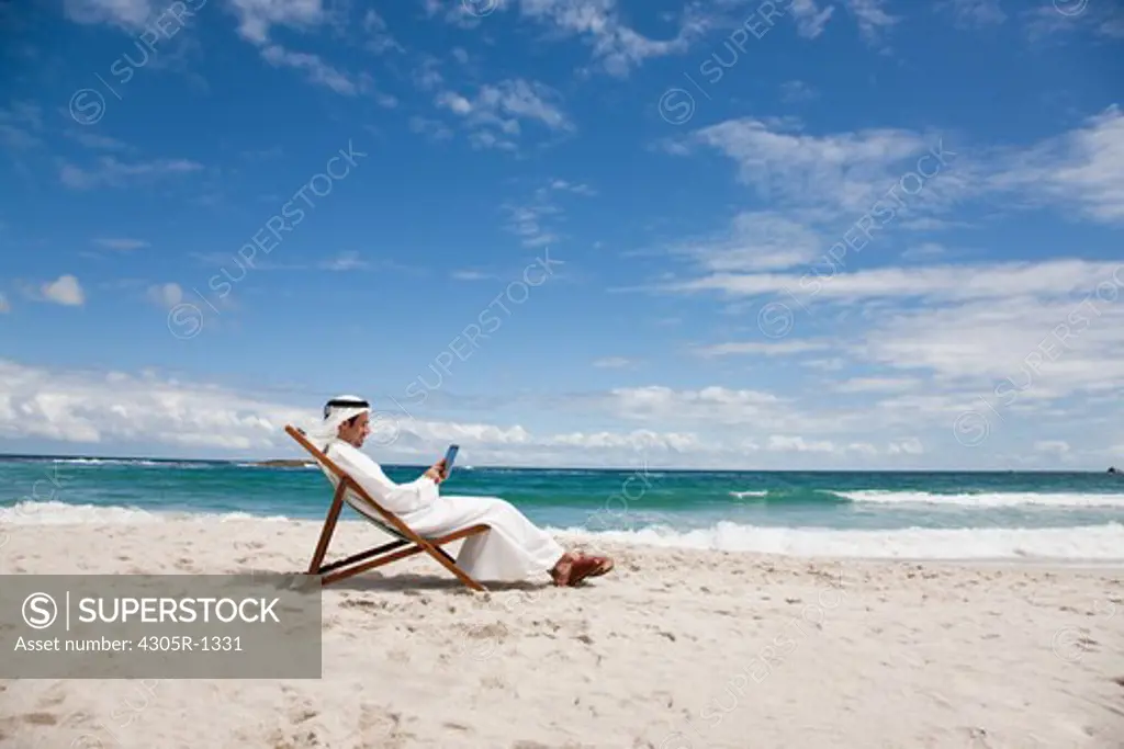 Arab man with digital tablet sitting at the beach.