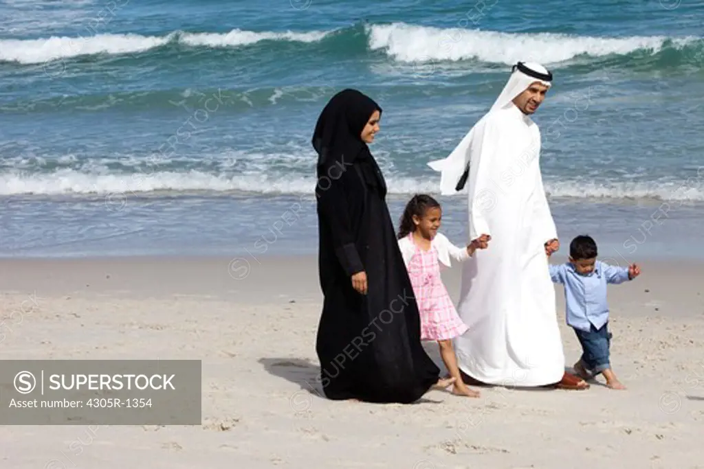 Arab family holding hands while walking at the beach.