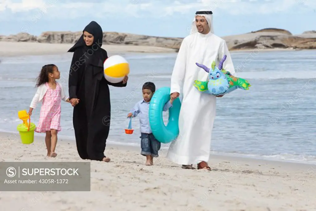 Arab family holding hands while walking at the beach.