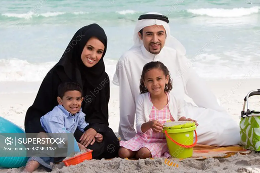 Arab family playing on the sand at the beach, smiling.