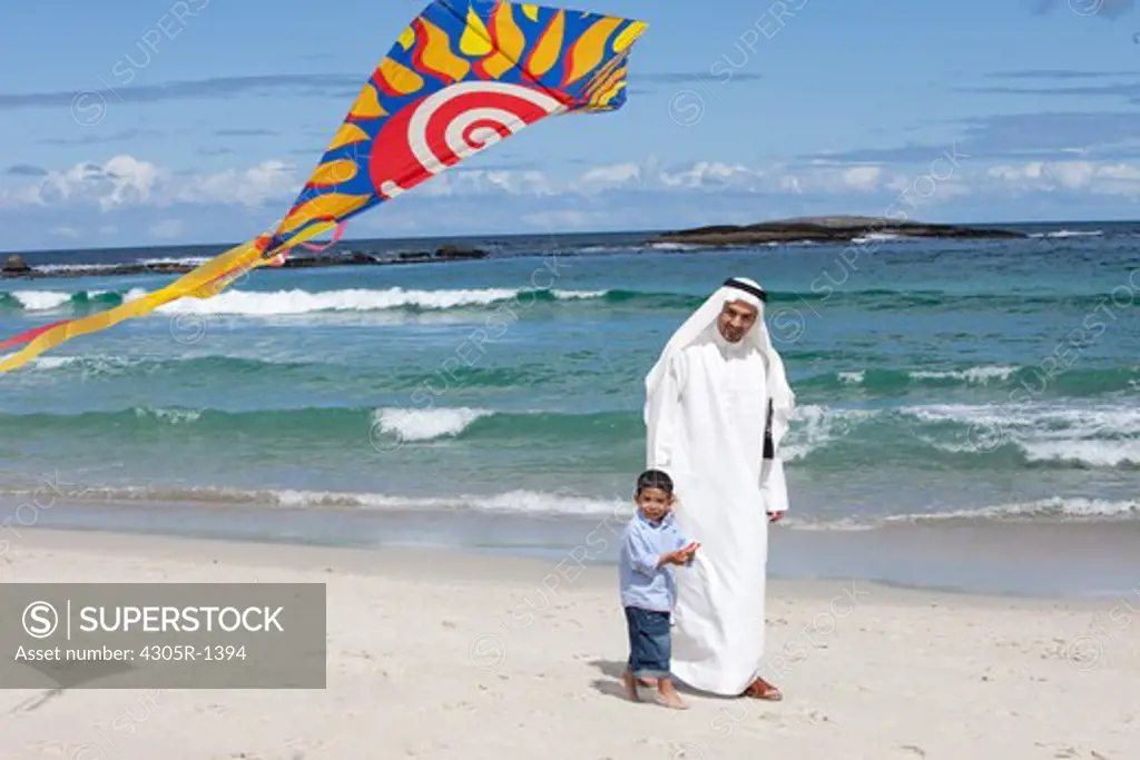Arab father and son with kite walking at the beach.