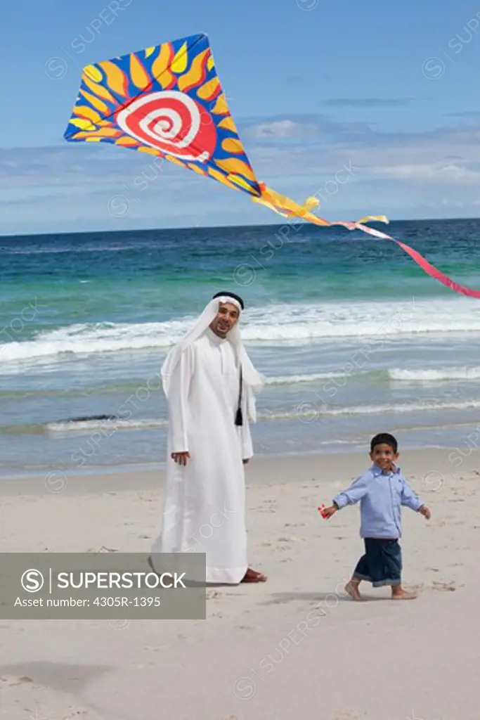 Arab father and son with kite walking at the beach.