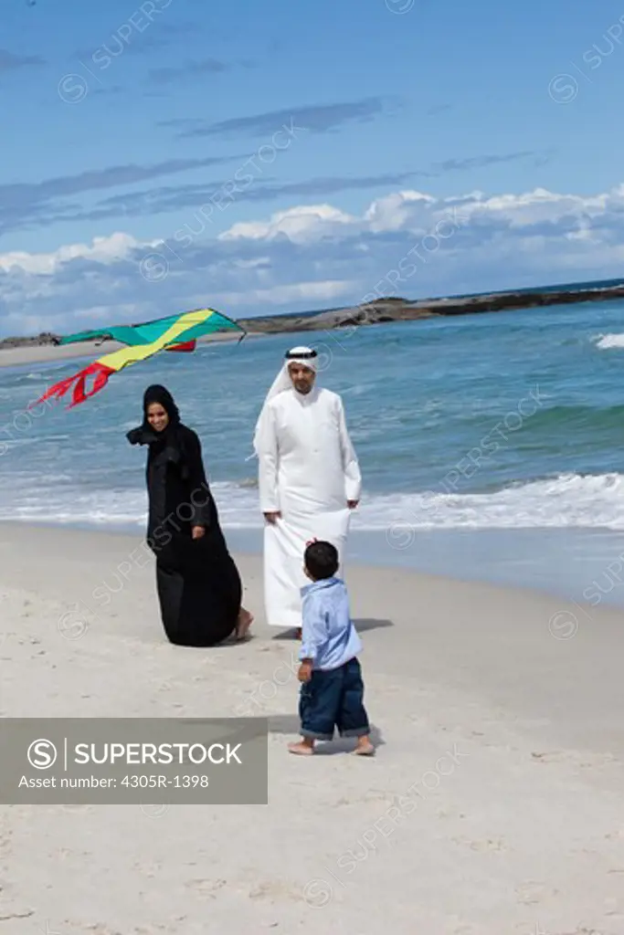 Arab family at the beach, son playing with kite.