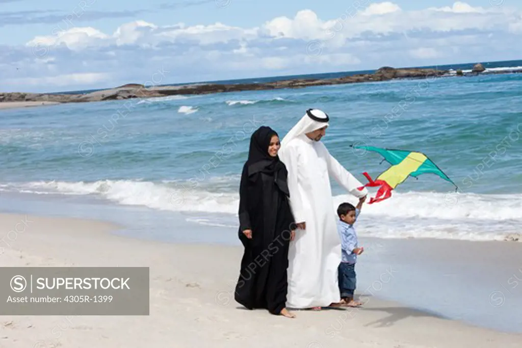 Arab family at the beach, son playing with kite.