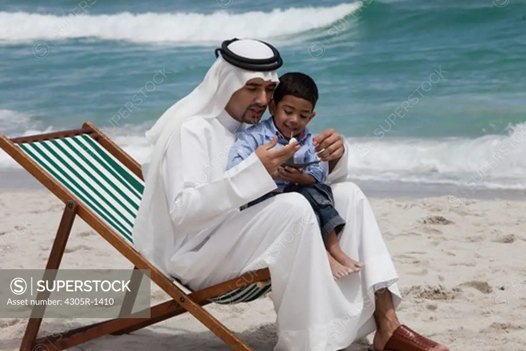 Arab father and son playing toy airplane at the beach.