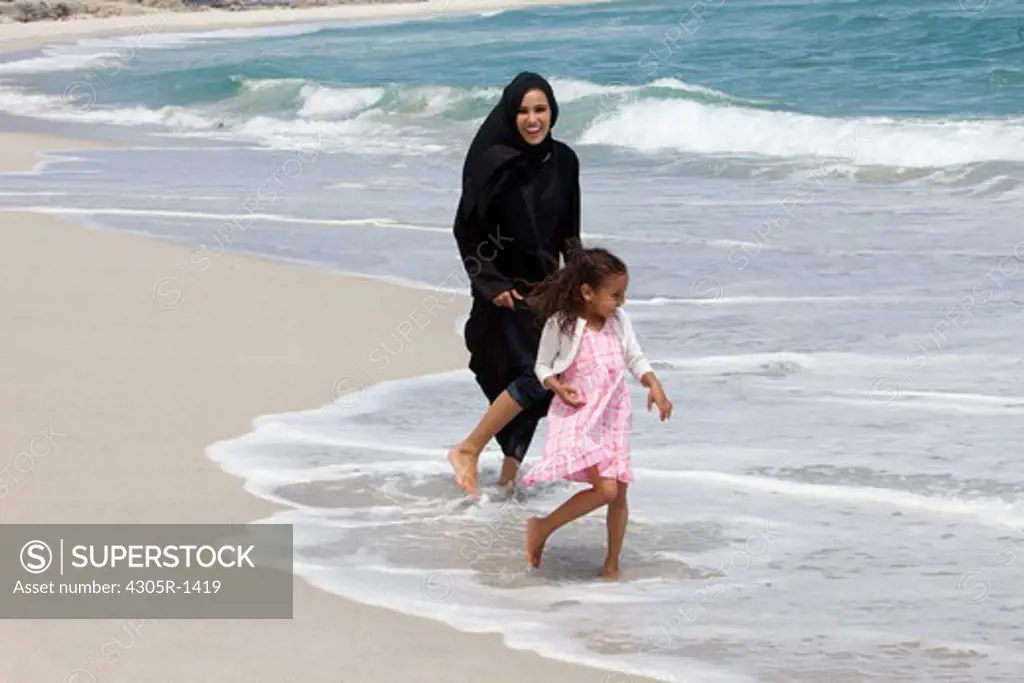 Arab mother and daughter playing at the beach.