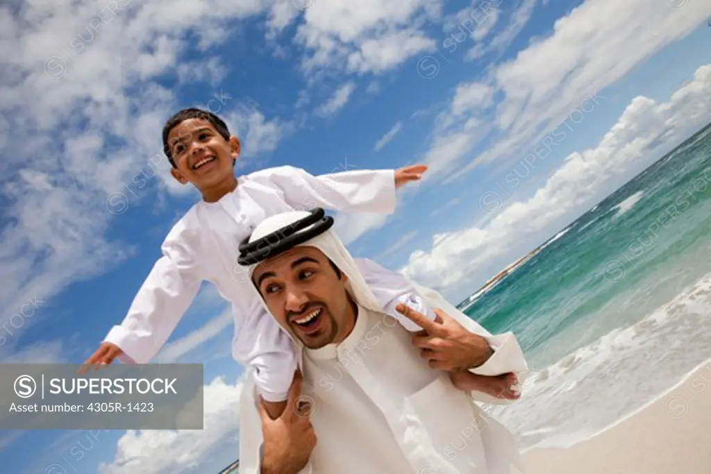 Arab father carrying his son on shoulders at the beach.