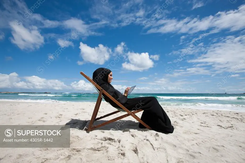 Arab woman with digital tablet sitting at the beach.