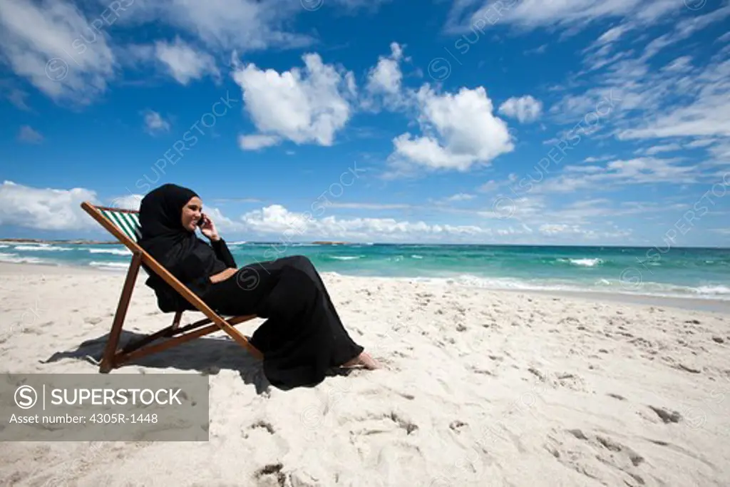 Arab woman with mobile phone sitting at the beach.
