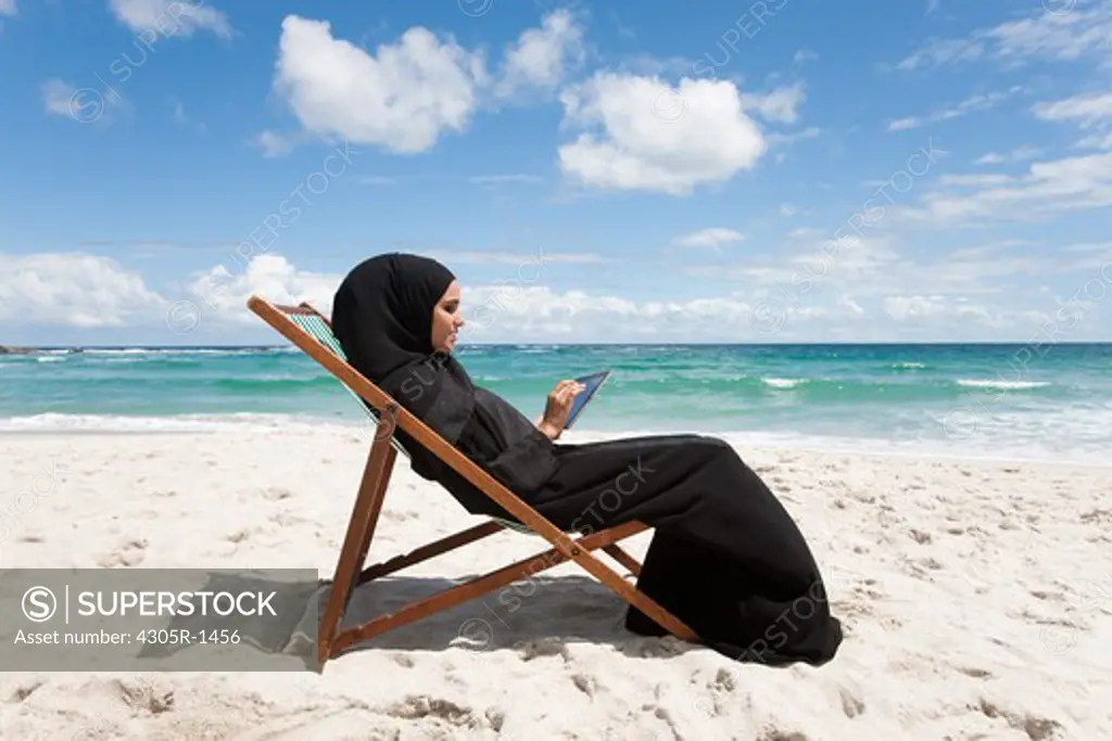 Arab woman with digital tablet sitting at the beach.