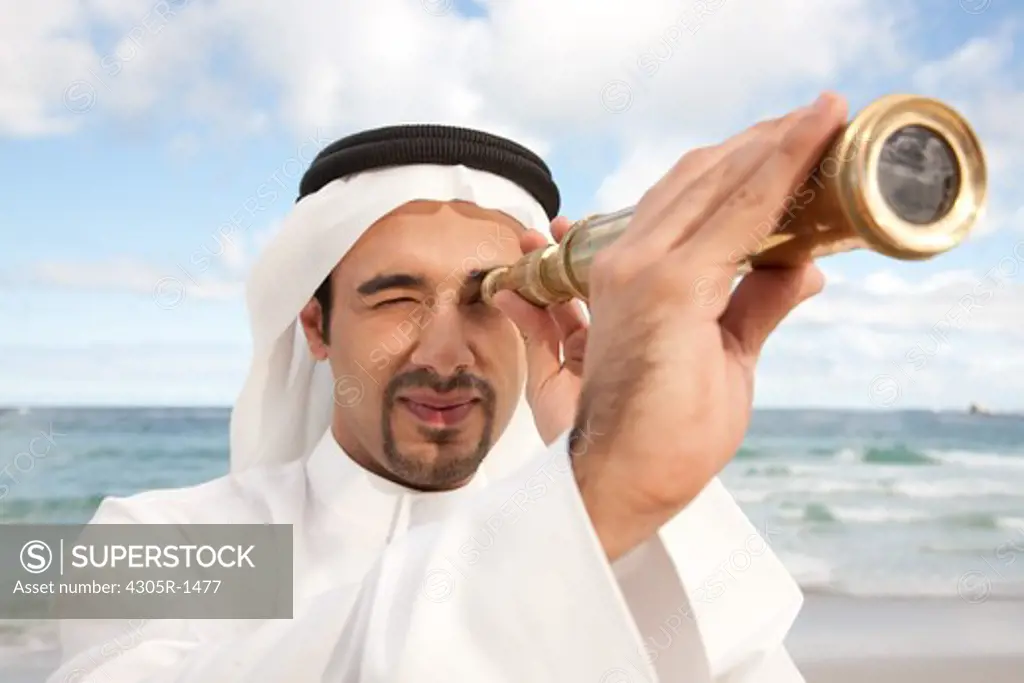 Arab man with telescope standing at the beach.