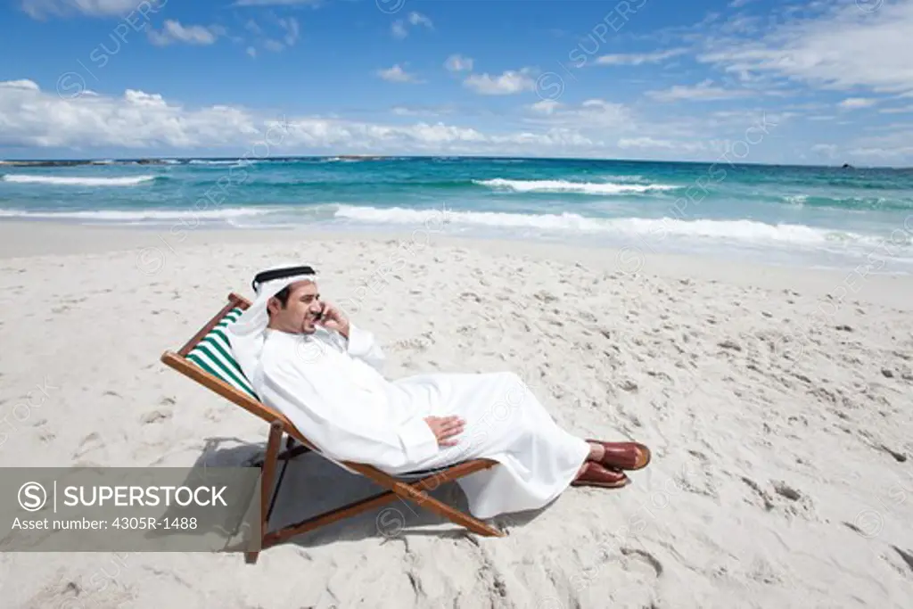 Arab man on the mobile phone sitting at the beach.
