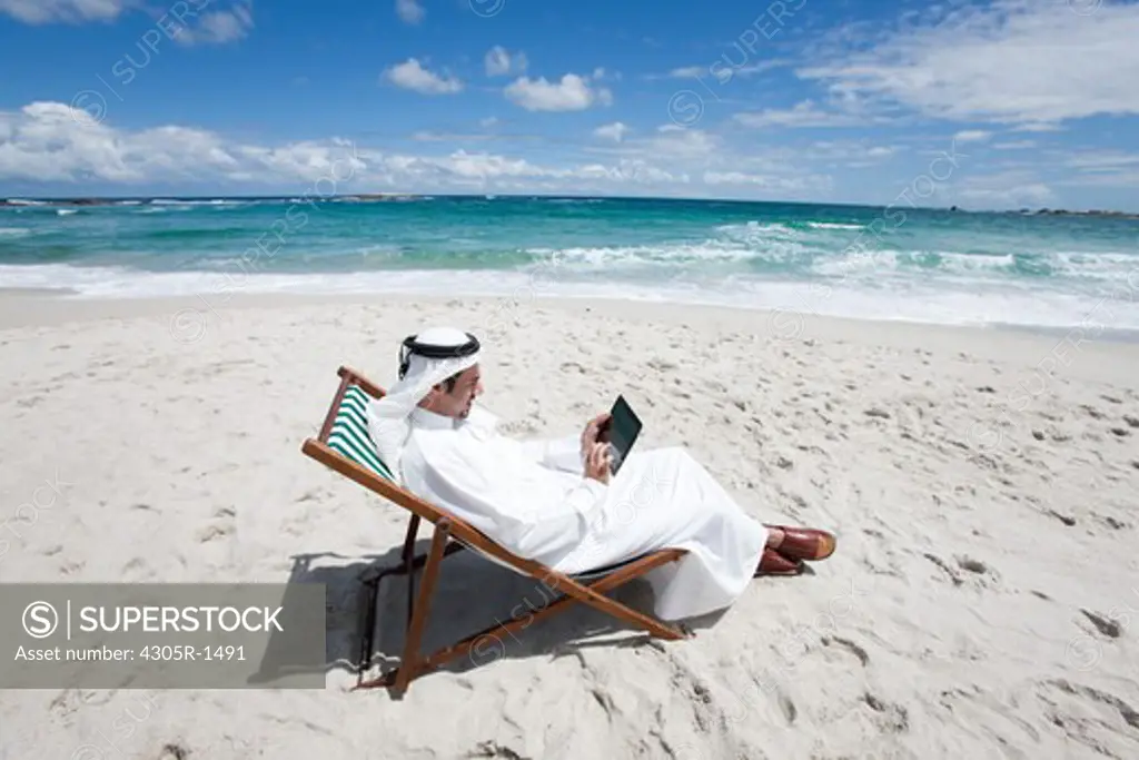 Arab man with digital tablet sitting at the beach.
