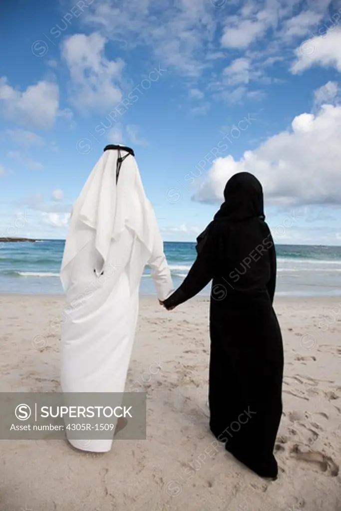 Rear view of arab couple holding hands at the beach.