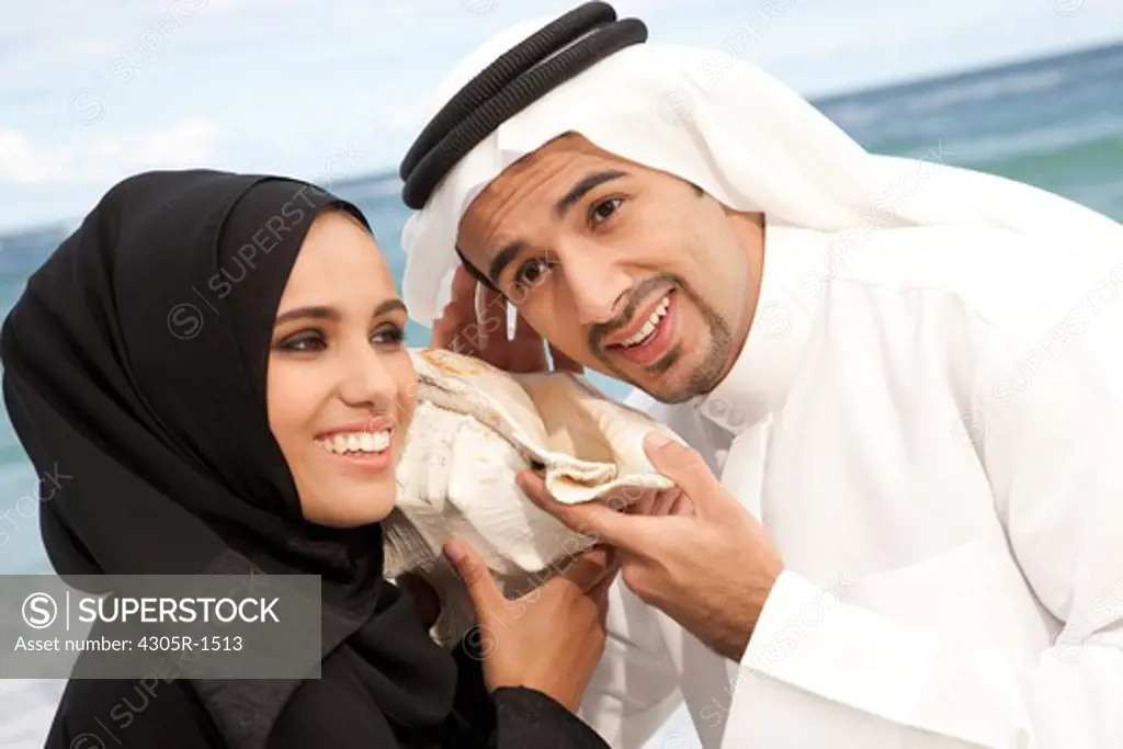 Arab couple listening to seashell together at the beach.