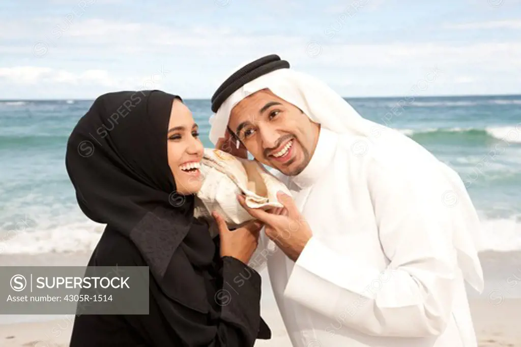 Arab couple listening to seashell together at the beach.