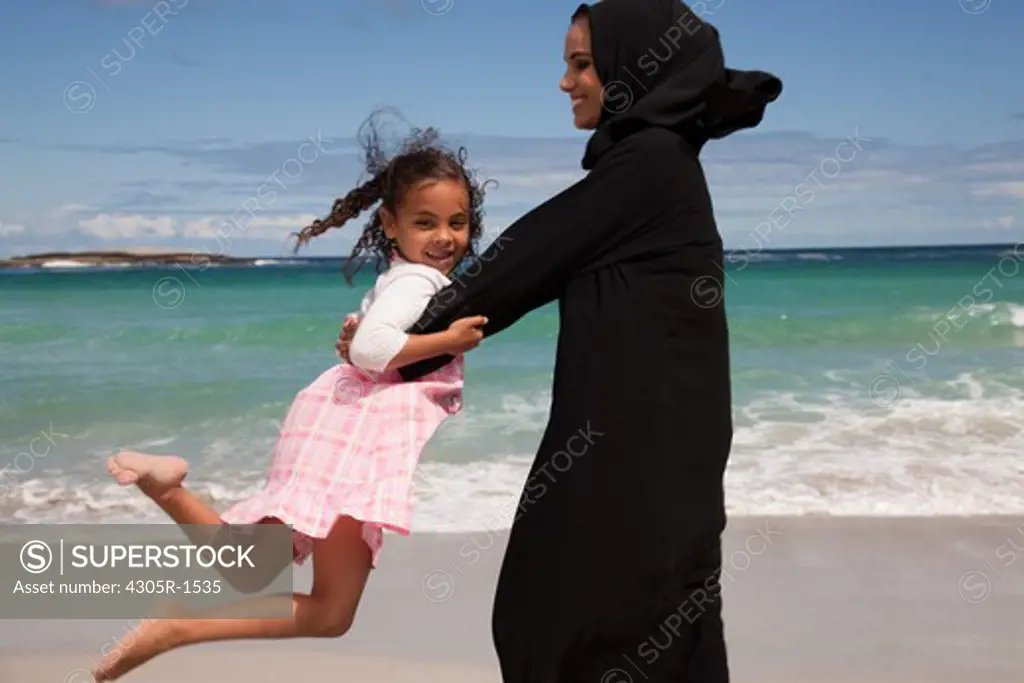 Arab mother spinning around her daughter at the beach.