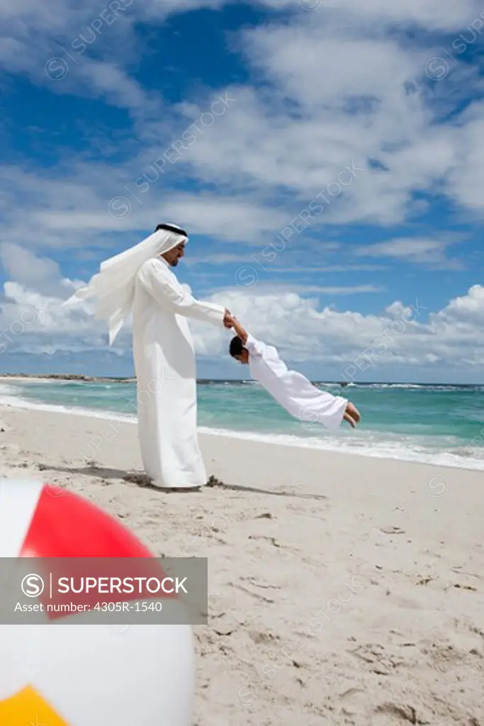 Arab father spinning around his son at the beach.
